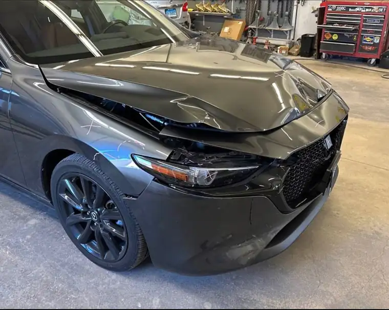 A grey Mazda3 with a crumpled hood and front bumper in the shop