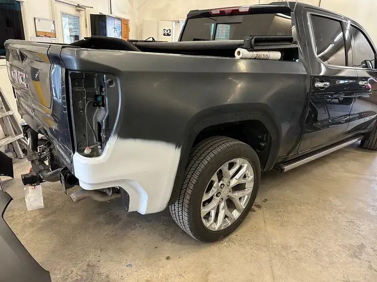 A black pickup with a primered rear quarter and missing tail light in the shop