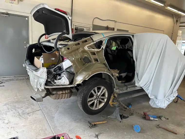 A silver sedan with its rear end cut back to structure in the shop