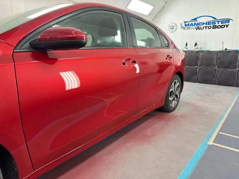 The same red sedan painted, in the Manchester Auto Body booth