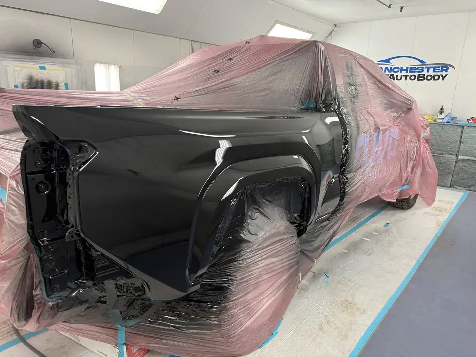 A black pickup bed freshly sprayed under pink masking film in the Manchester Auto Body paint booth