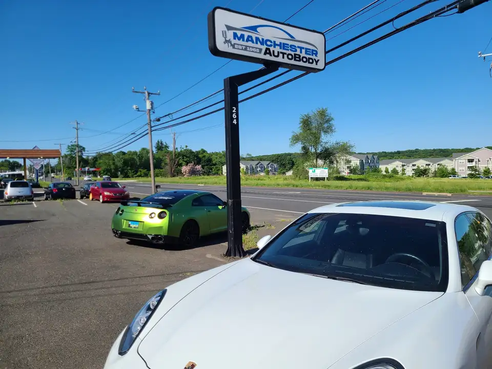 A lime green wrapped Nissan GT-R beside the Manchester Auto Body roadside sign on Talcottville Road