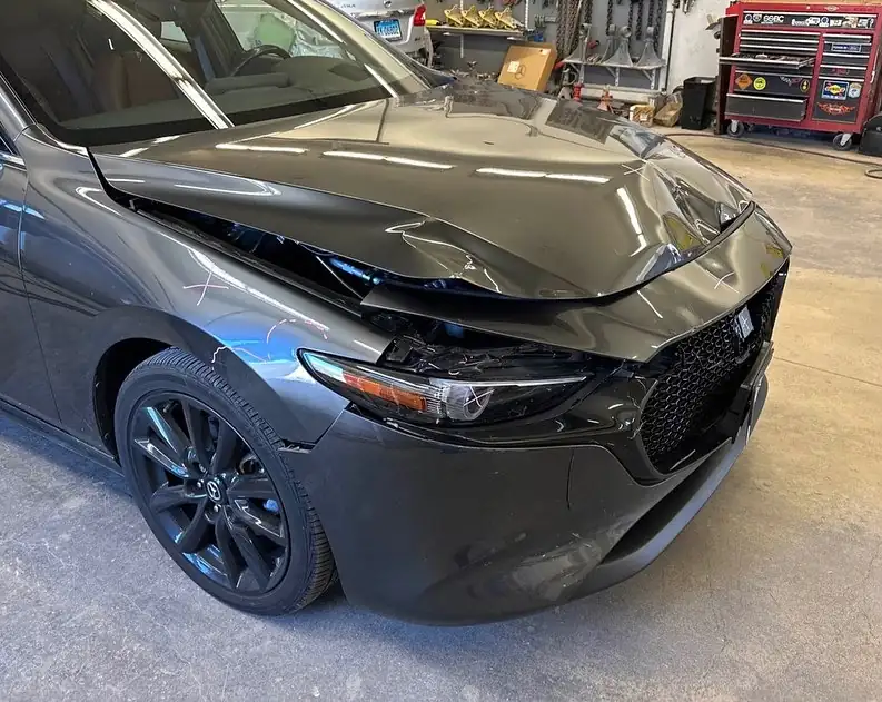 A Mazda3 with a crumpled hood and front bumper after a collision, at Manchester Auto Body